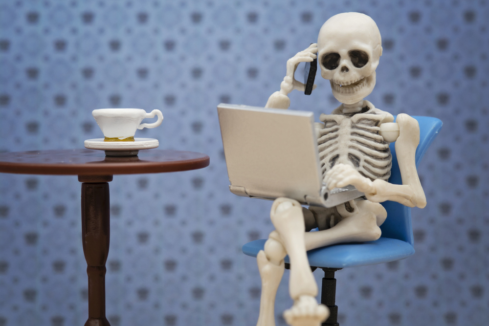 A skeleton takes a call while working on its laptop at a cafe
